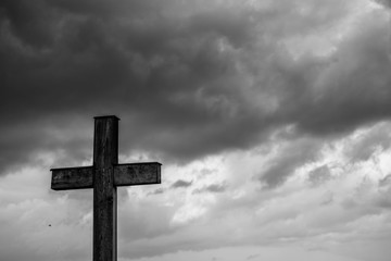 Simple oak catholic cross, storm clouds in the background, space for text in black and white.