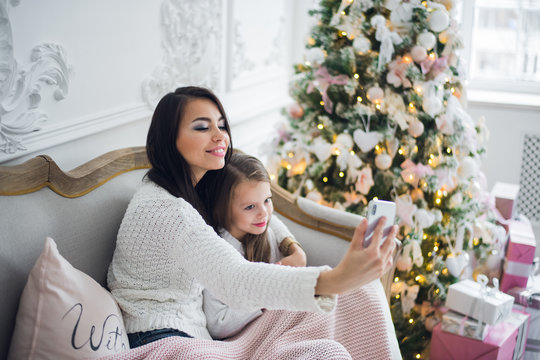 Happy mother and daughter taking funny Christmas selfies at home