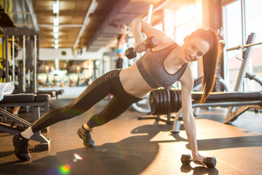 Fitness woman in activewear doing one-hand push ups with weights at gym - Powered by Adobe