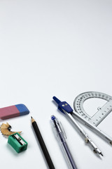 A close-up photo of stationary set: pen, pencil, compass, rubber, protractor and etc. on the white background on the table in office, school or university. A workspace of student or an office worker.