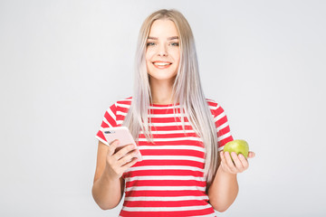 Portrait of a beautiful young woman holding an apple and phone on a white background.