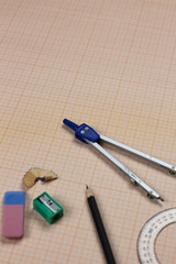 A close-up photo of stationary set: pen, pencil, compass, rubber, protractor, calipers and etc. on the graph paper background on the table in office, school or university. A workspace of student.