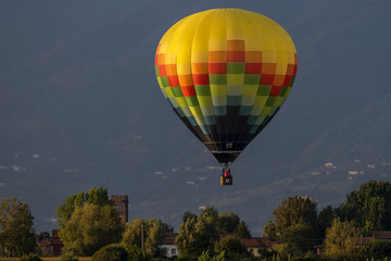 Colorful hot-air balloon flies over typical village in the Tuscan countryside in the light of the...