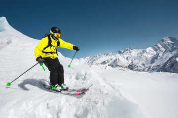 Professional skier at the speed before jumping from the glacier in winter against the blue sky and...