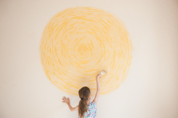 talented small caucasian girl painting yellow sun on wall with brush