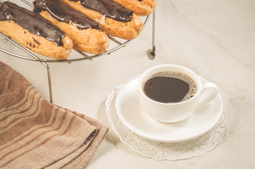 fresh eclairs with chocolate and a coffee cup/fresh eclairs with chocolate and a coffee cup on a white marble background.