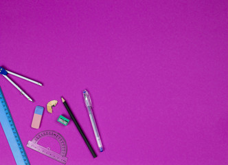 A photo of stationery set: pen, rubber, sharpener, compass, protractor, ruler,  and etc. on the pink background on the table . Workspace of student or office worker.