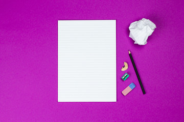 A flat lay photo of stationery set: notebook,crumpled paper ball pencil,and sharpener  on the pink background on the table in the office or school or university. Workspace of student or office worker.