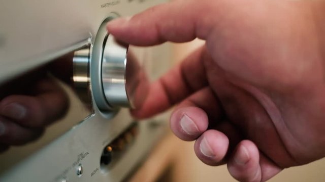 Man's hand turning a dial to increase and decrease volume on hifi stereo, close up shot