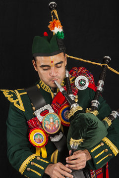 A portrait of an Indian American Scottish bagpiper playing the bagpipe and looking away camera in full Scottish regalia, including kilt and sporrans