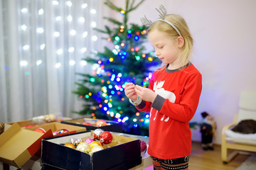 Adorable little girl decorating the Christmas tree with colorful glass baubles. Trimming the Christmas tree.