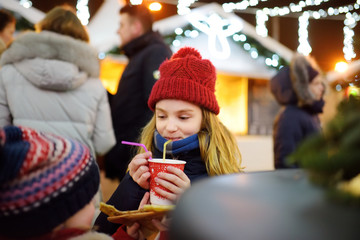 Two adorable sisters drinking hot chocolate on traditional Christmas market.