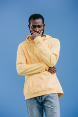 worried young african american man with hand on chin solated on blue background