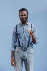 grimacing african american man holding condom isolated on blue