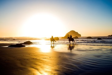 Two people riding horses on a beach off into the sunset - 221859462