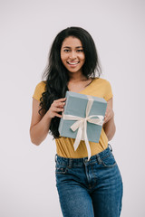 smiling african american girl holding present box and looking at camera isolated on white