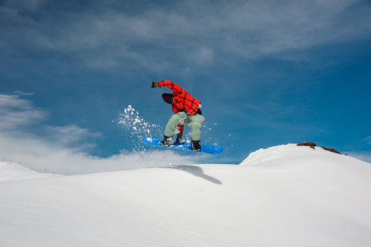 guy is jumping on a blue snowboard from a snowy mountain
