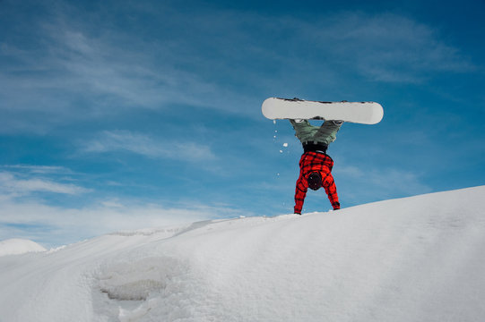 guy stands on his hands in the snow against a blue winter sky