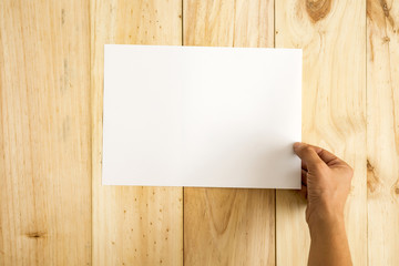 Mano sujetando un papel A4 preparado para insertar texto sobre fondo de madera