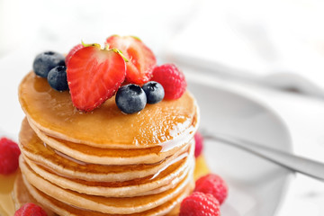 Tasty pancakes with berries and honey on plate, closeup