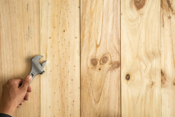 Mano de trabajador sujetando una llave inglesa preparado para reparar sobre fondo de madera