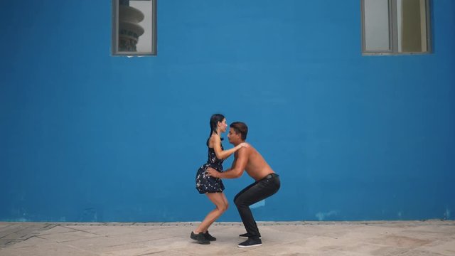 Dance partners demonstrating sensual dance pattern with acrobatics in slow motion on blue background. Dancing outdoors in the city