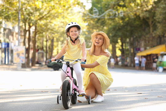 Mother teaching daughter to ride bicycle on street