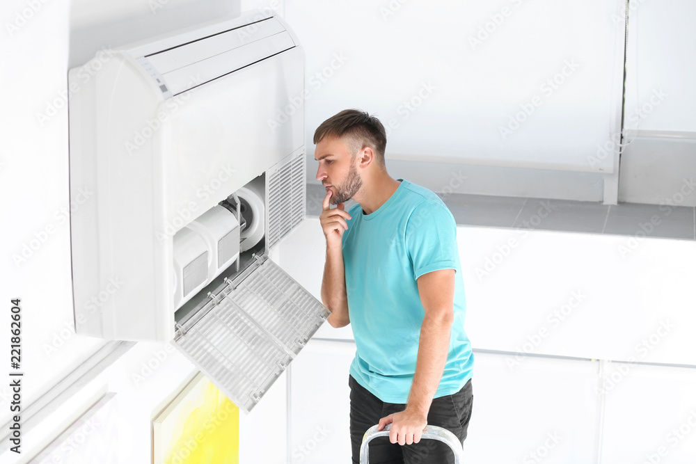 Poster young man fixing air conditioner at home