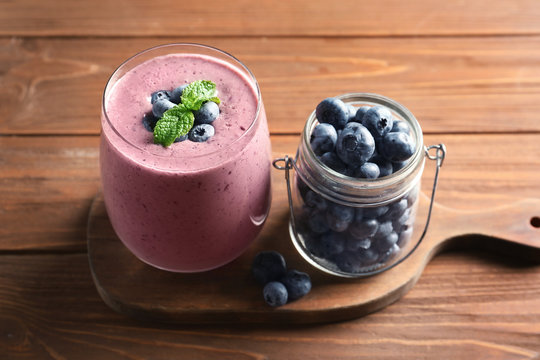 Glass of smoothie and jar with blueberries on wooden background
