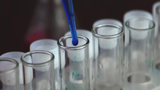 In a laboratory, a scientist with a pipette analyzes a blue liquid to extract the DNA and molecules in the test tubes. Doctor working with liquid.
