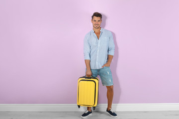 Fototapeta na wymiar Young man with suitcase on color wall background
