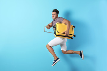 Young man jumping with suitcase on color background