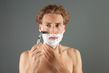 Handsome young man shaving on gray background