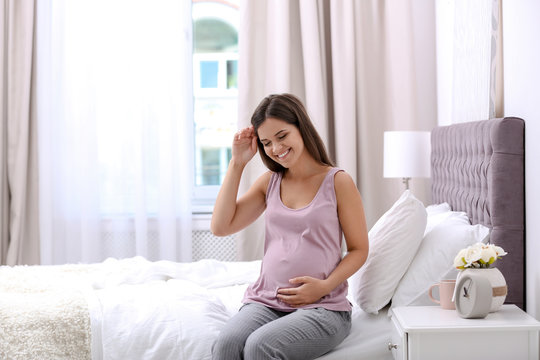 Happy pregnant woman sitting on bed at home