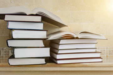 Pile of books with open book on marble shelf. Bookshelf with piled books.