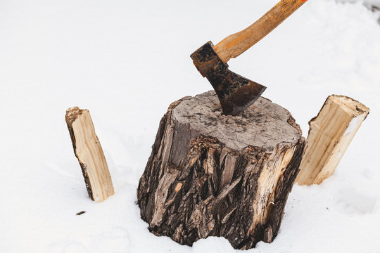 ax sticks out in stump against background of white snow