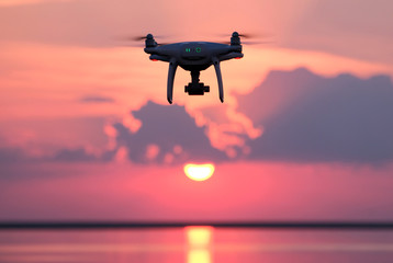 Naklejka na ściany i meble Unmanned aerial vehicle on a background of pink clouds. Silhouette of radio-controlled drone over the water surface at sunset. The concept of heavenly photography and video.