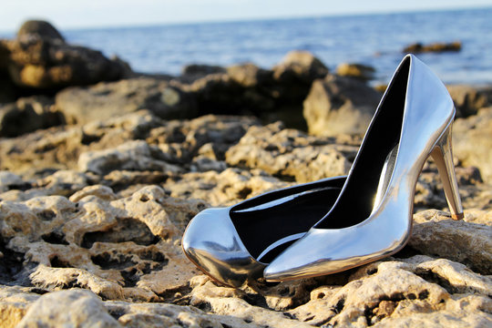 Close-up shot of Pair of Silver High Heel Shoes on yellow stones near sea © Valeriia
