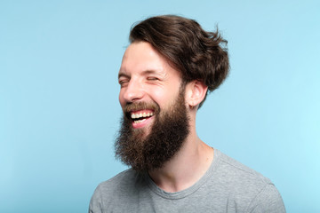 Fototapeta premium emotional facial expression. happy joyful smiling man. young handsome bearded hipster guy portrait on blue background.