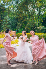 Fototapeta na wymiar Bride and bridesmaid in nature with bouquets of flowers. Funny wedding moments, bride show bridesmaids her new ring. Girls in shock.