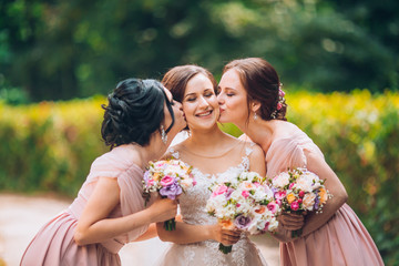 Bride and bridesmaid in nature with bouquets of flowers. Funny wedding moments, bride show bridesmaids her new ring. Girls in shock.