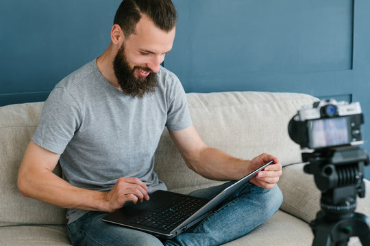 content creation for social media. bearded man holding laptop and shooting video of himself using camera on tripod. modern technology and blogging freelance work concept.