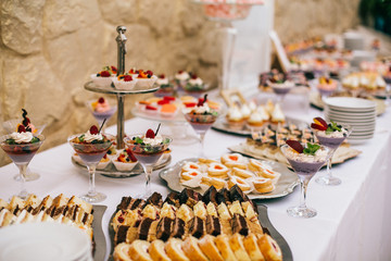 Candy bar. White wedding cake decorated by flowers standing of festive table with deserts, strawberry tartlet and cupcakes. Wedding. Reception Tartlets