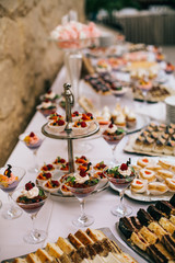 Candy bar. White wedding cake decorated by flowers standing of festive table with deserts, strawberry tartlet and cupcakes. Wedding. Reception Tartlets