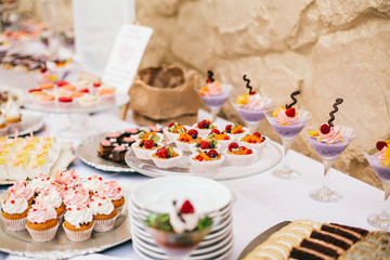 Candy bar. White wedding cake decorated by flowers standing of festive table with deserts, strawberry tartlet and cupcakes. Wedding. Reception Tartlets