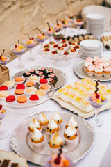 Candy bar. White wedding cake decorated by flowers standing of festive table with deserts, strawberry tartlet and cupcakes. Wedding. Reception Tartlets