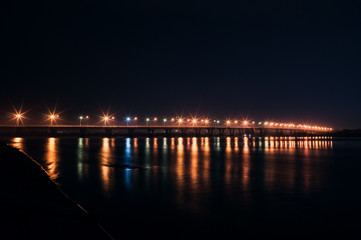 Fototapeta na wymiar The lights of the bridge over the river at night