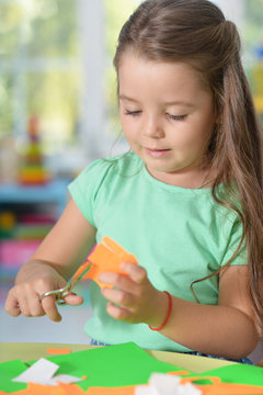 Portrait of little girl is cutting color paper