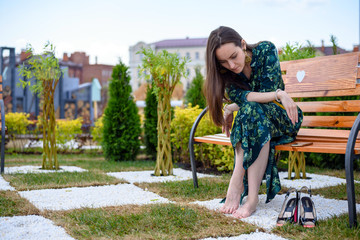 Young woman sitting on bench barefoot next to high heel shoes, rest from shoes