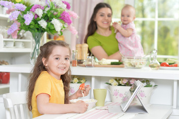 Cute little girl eating fresh salad at kitchen table
